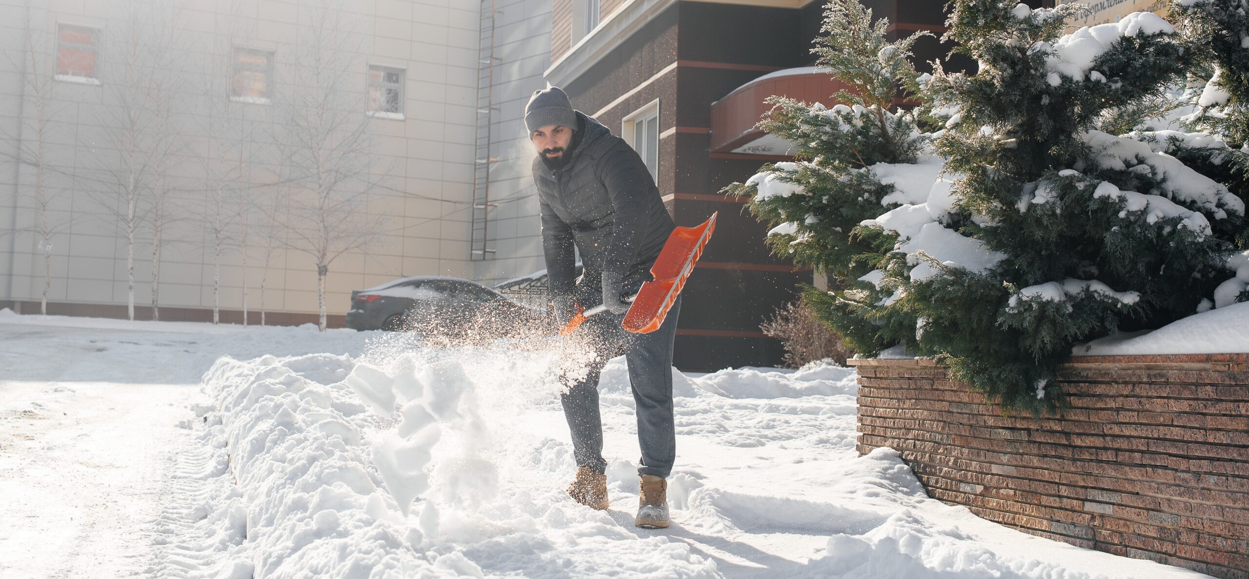 A man shoveling snow, wearing thick layers to prevent hypothermia.