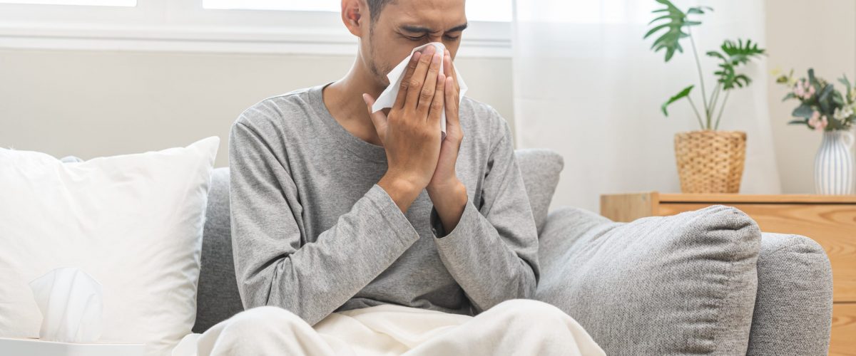 A person blowing their nose into a tissue on a couch